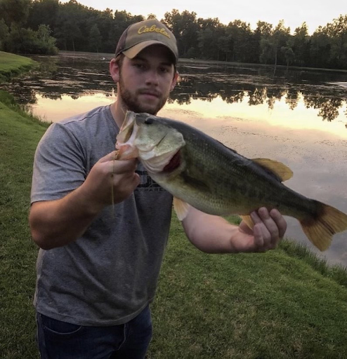 Young man hold a huge largemouth bass that he just caught, with pond in background.